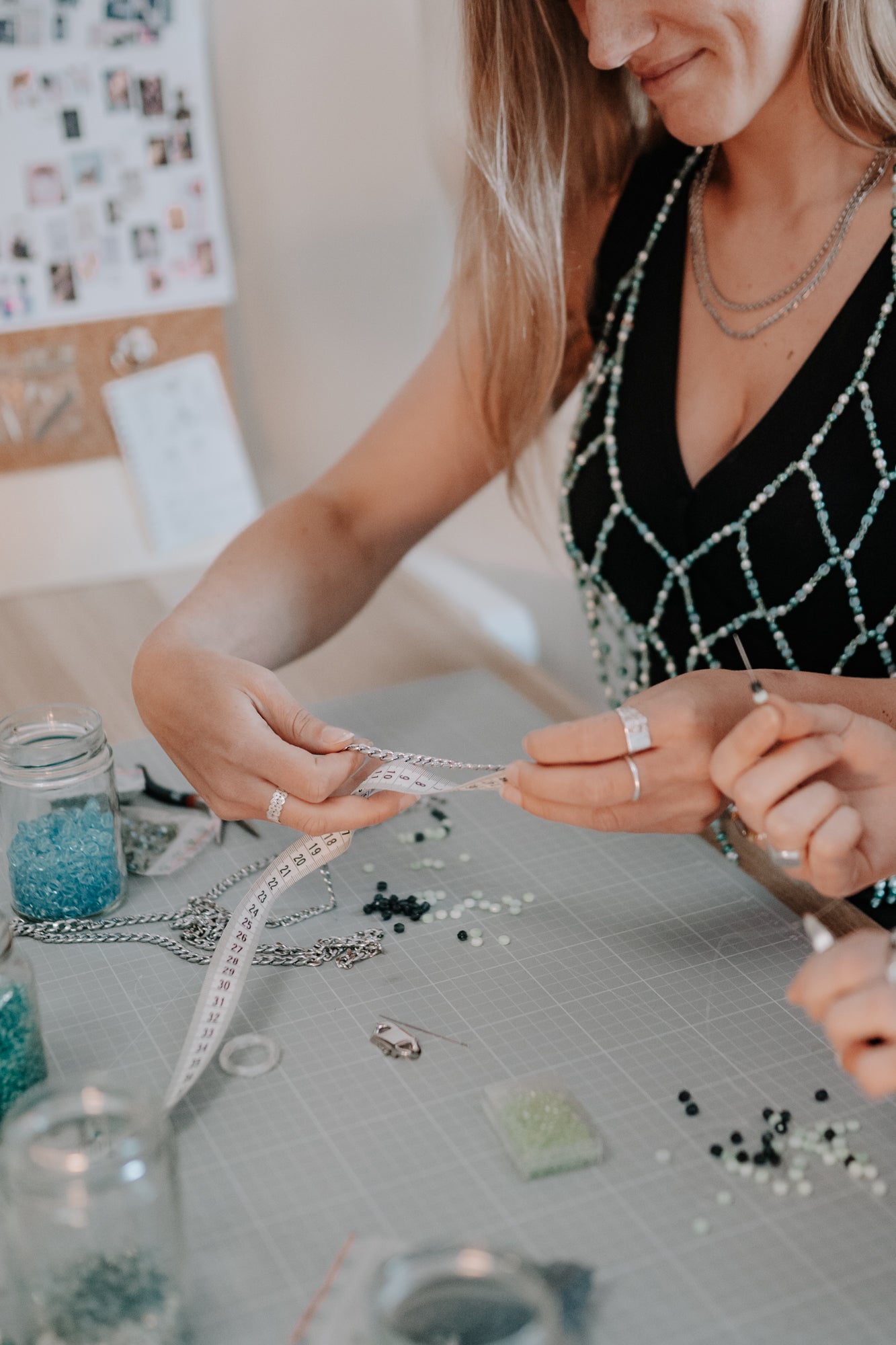 arah Hanisch (Gründerin von SOIRA) bei der Arbeit an Produkten. Sitzend am Tisch mit Perlen und Edelstahl Materialien. Im Hintergrund Inspirationsboards der Firma SOIRA