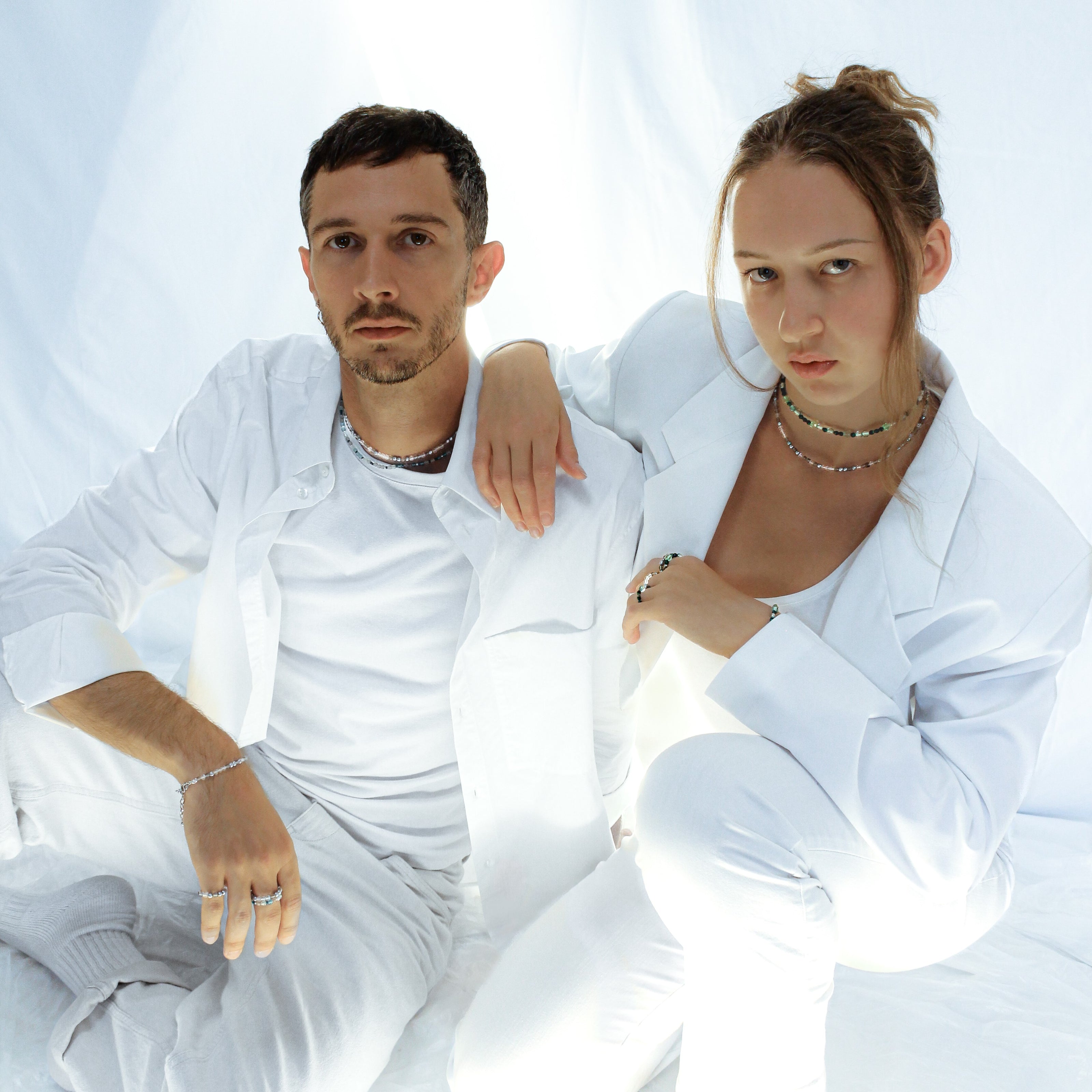 Azure Collection Photo of female model Luisa Hill and male model Jerome Dureault wearing SOIRA jewlry. Models are dressed in white in front of white background. SOIRA necklace, rings, bracelets